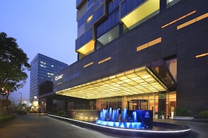 A modern hotel with a glass facade, a covered entrance, and a water feature in front. - The Qube Hotel Shanghai Pudong (Shanghai)
