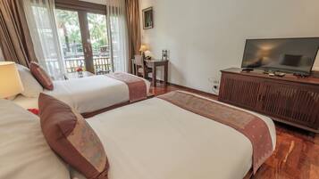 A hotel room with two beds, a television, a desk with a chair, and a view of palm trees through the window.
