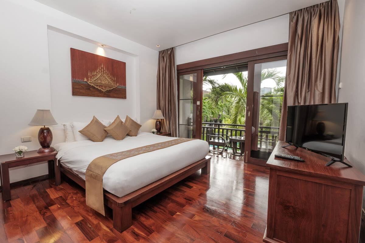 Une chambre dotée d’un grand lit, d’un plancher en bois, d’un téléviseur posé sur un meuble en bois et d’un balcon offrant une vue sur la verdure.