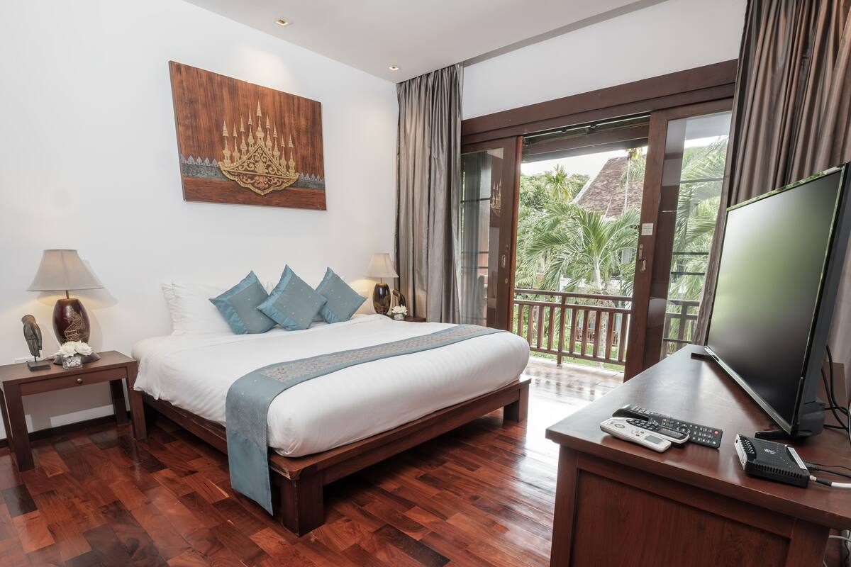 Une chambre d’hôtel avec un grand lit, un bureau avec une télévision et un balcon offrant une vue sur les palmiers.