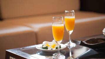 Two glasses of orange juice on a table with a plate of flowers and a woven basket.