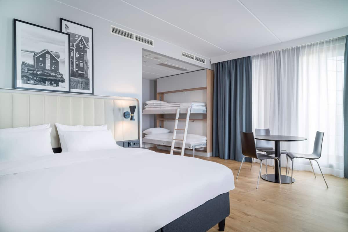 Une chambre d’hôtel avec un grand lit, un lit superposé, un bureau avec des chaises et une table à manger.