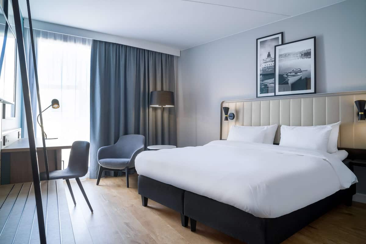 Une chambre d’hôtel avec un grand lit, un bureau, une chaise et une fenêtre avec des rideaux.