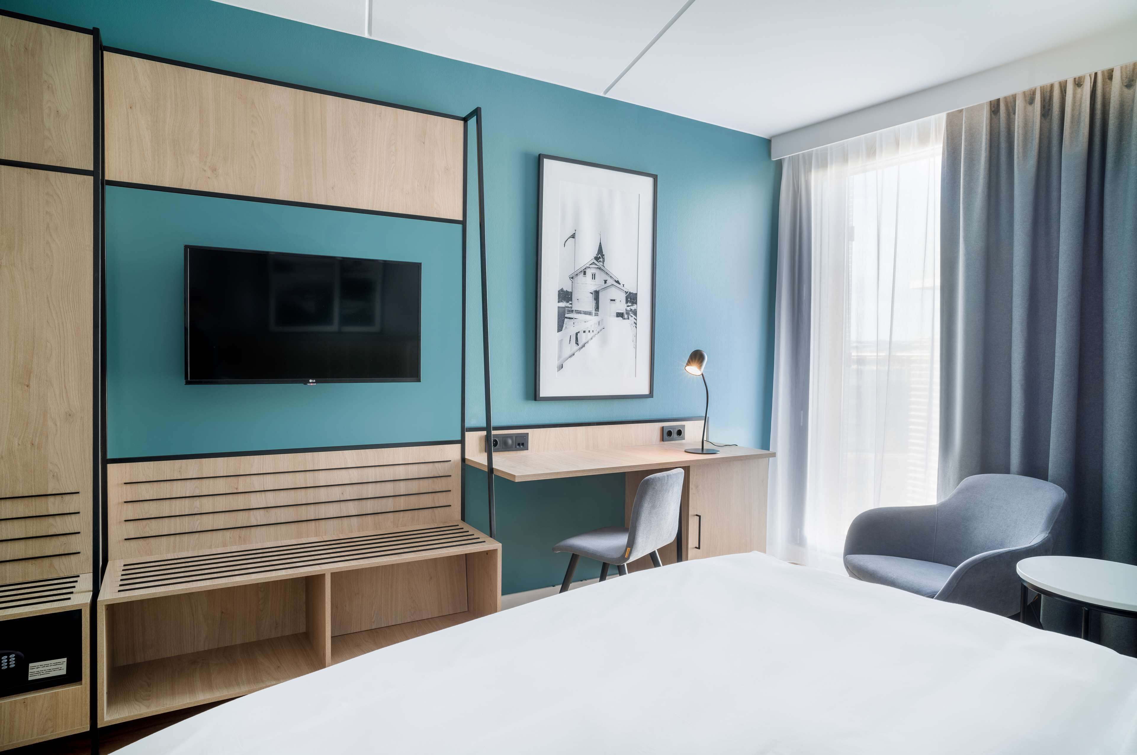 Una habitación de hotel moderna con una cama grande, un escritorio, una silla, un televisor y un cuadro en la pared.