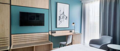 Una habitación de hotel moderna con una cama grande, un escritorio, una silla, un televisor y un cuadro en la pared.