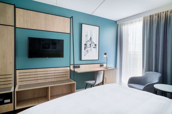 Une chambre d’hôtel moderne, dotée d’un grand lit, d’un bureau, d’une chaise, d’une télévision et d’un tableau encadré au mur.