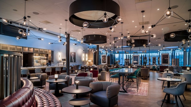 Un espace de détente moderne avec des sièges en cuir, des tables rondes et des luminaires suspendus.