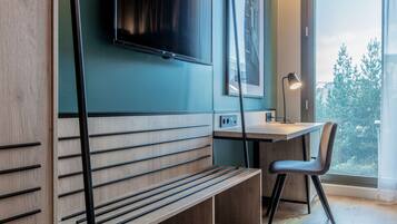 A modern room with a wooden bench, a desk, a chair, a TV mounted on the wall, and a window with a view of trees.