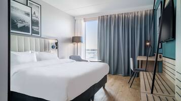 Een hotelkamer met een groot bed, een bureau, een stoel, een televisie en een raam met gordijnen.