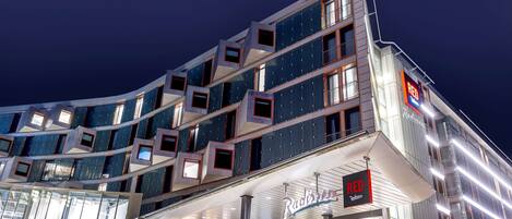 A modern building with a curved facade, multiple balconies, and a prominent 'RED' sign indicating a restaurant.