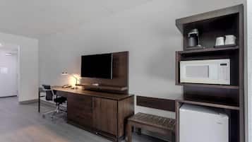 A hotel room with a wooden desk, a television, a microwave, a bench, and a refrigerator.