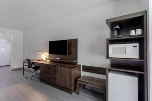 Habitación de hotel con escritorio de madera, televisor, microondas, banco y refrigerador.