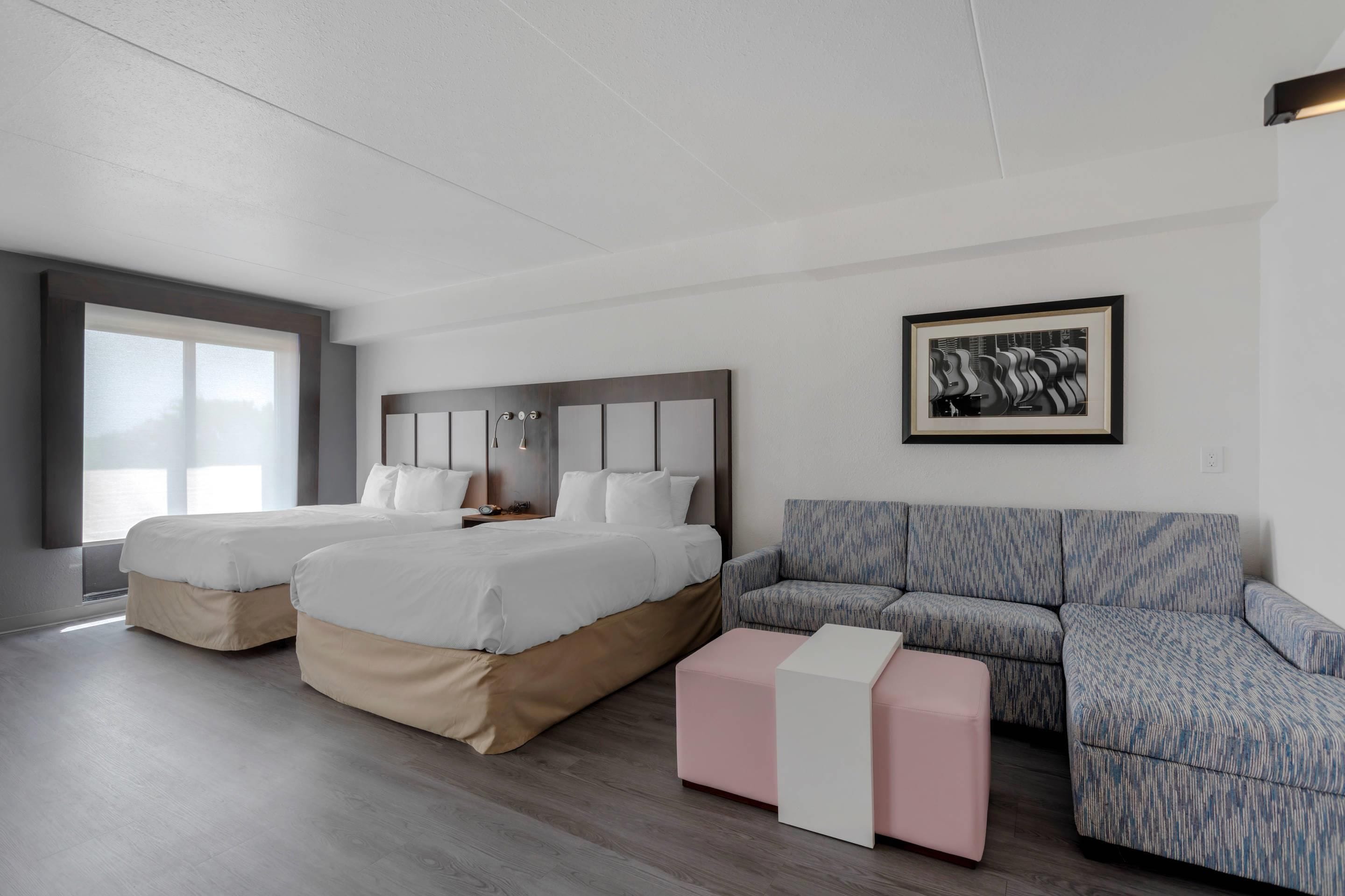 Une chambre d’hôtel moderne avec deux lits, un canapé et un tableau encadré au mur.