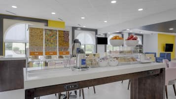 Un bar à petit-déjeuner moderne, équipé d’une machine à café, de corbeilles de fruits et d’une variété de viennoiseries.