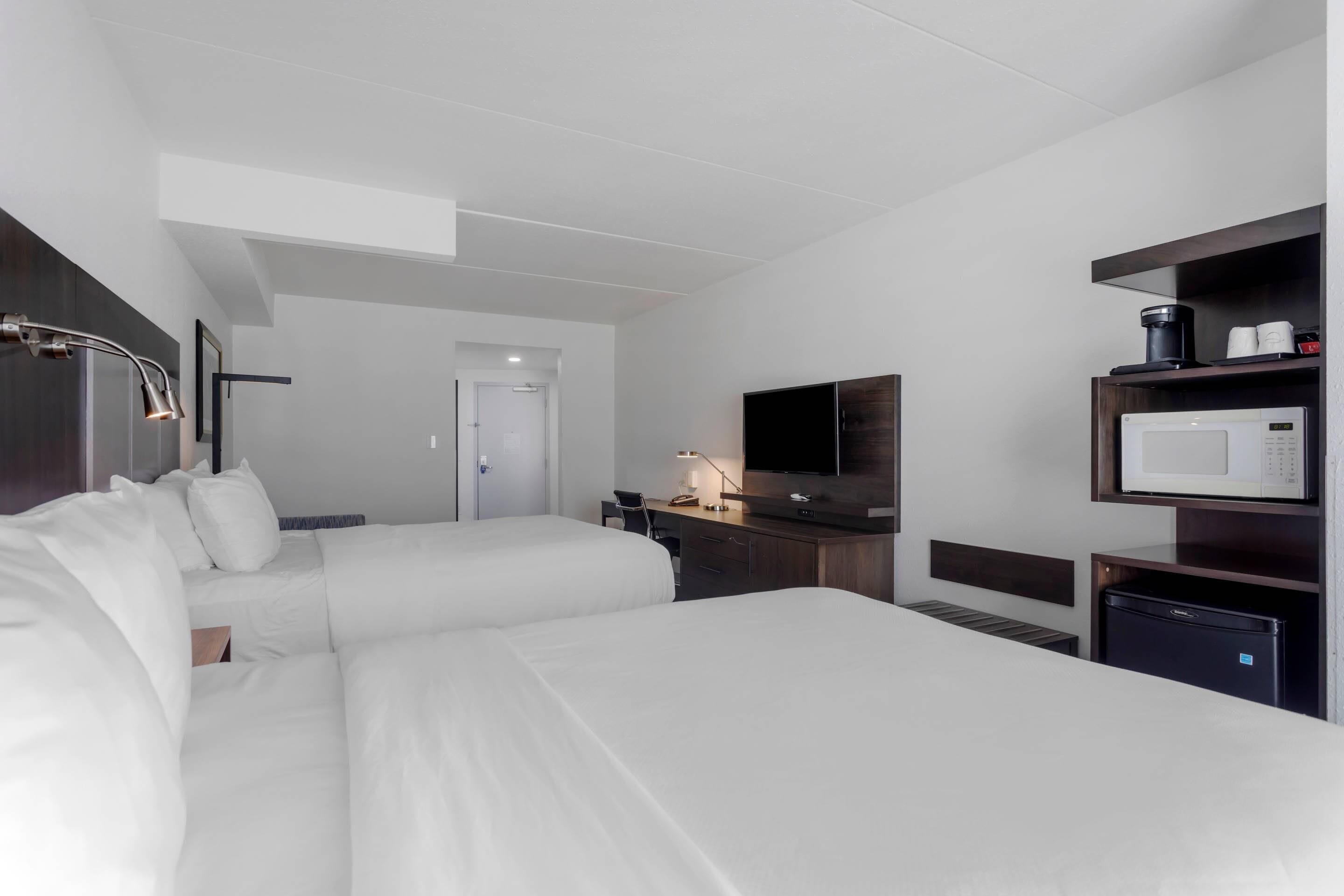 A hotel room with two beds, a desk, a flat-screen TV, a microwave, and a coffee maker.