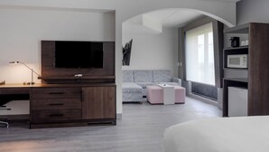Una habitación de hotel moderna con un escritorio de madera, un televisor de pantalla plana, un sofá y un microondas.
