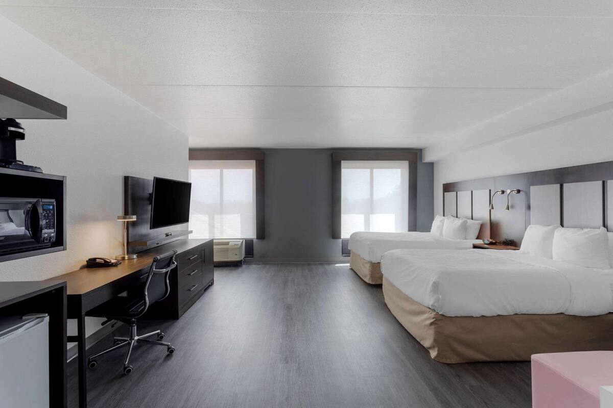 A hotel room with a desk, TV, two beds, and a large window.