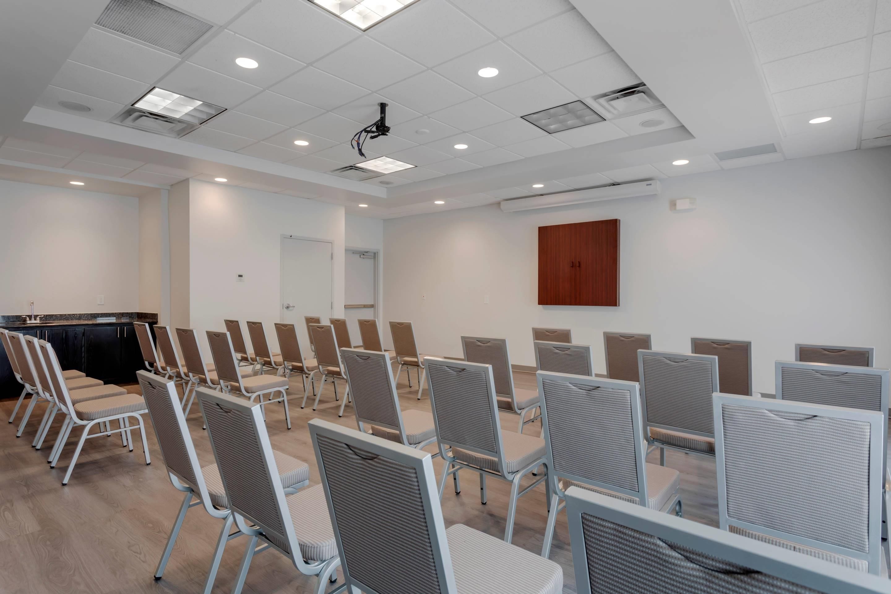 A conference room with rows of chairs, a projector, and a wooden panel on the wall.