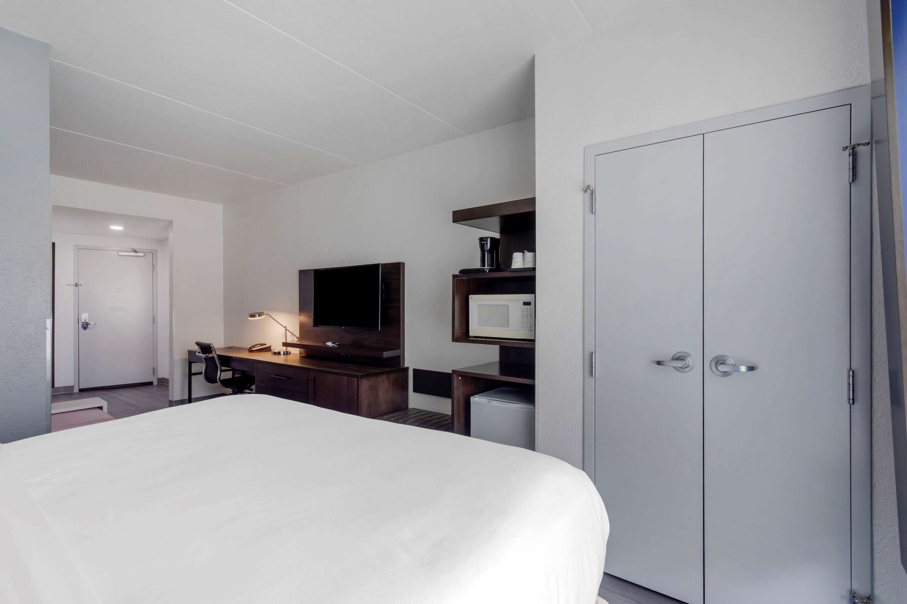 A hotel room with a large bed, a desk with a computer, a TV, a microwave, and a wardrobe.