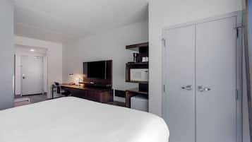 A hotel room with a large bed, a desk with a computer, a TV, a microwave, and a wardrobe.