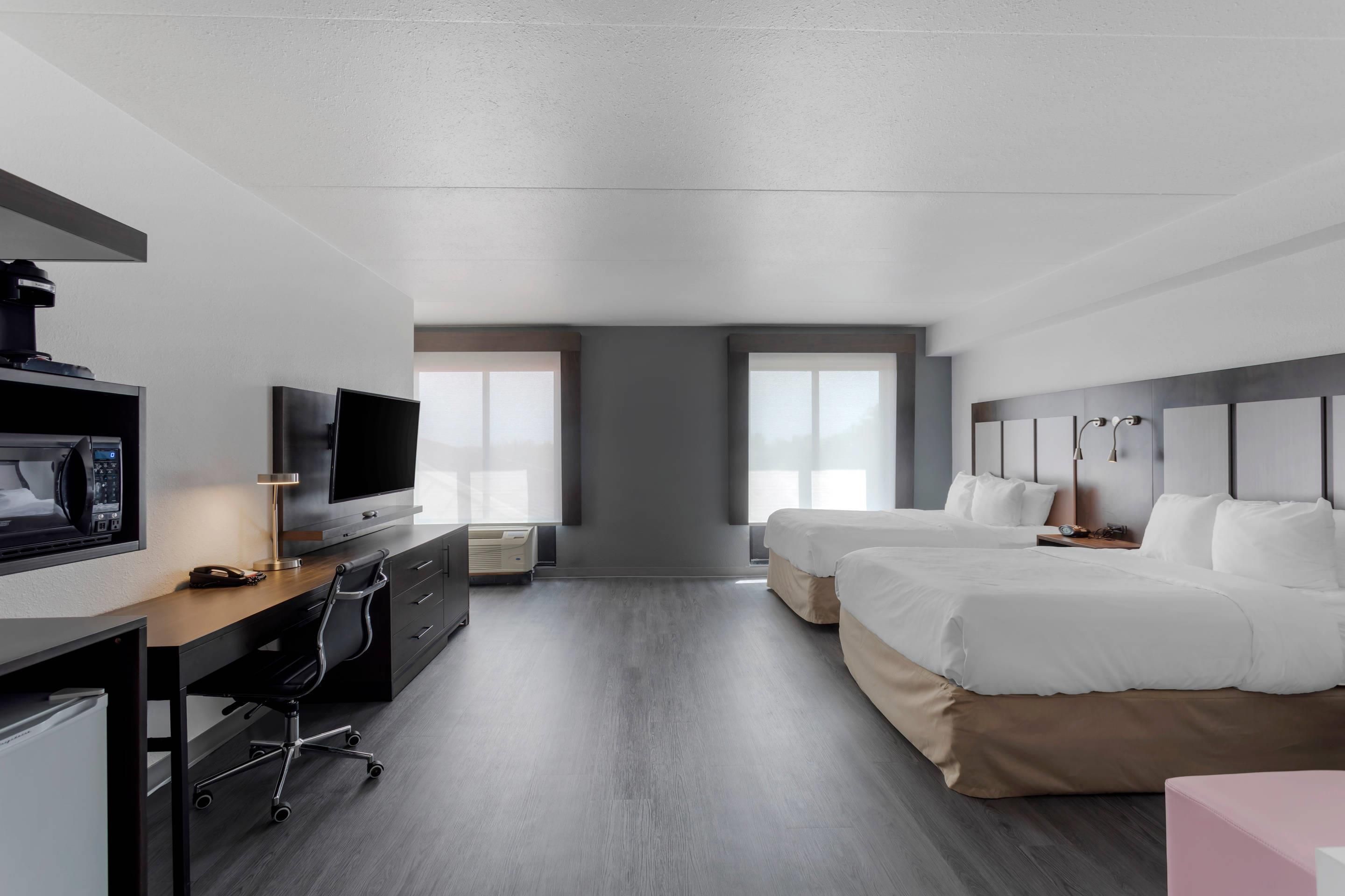 A modern hotel room with a flat-screen TV, a desk with a lamp, two beds, and a large window.