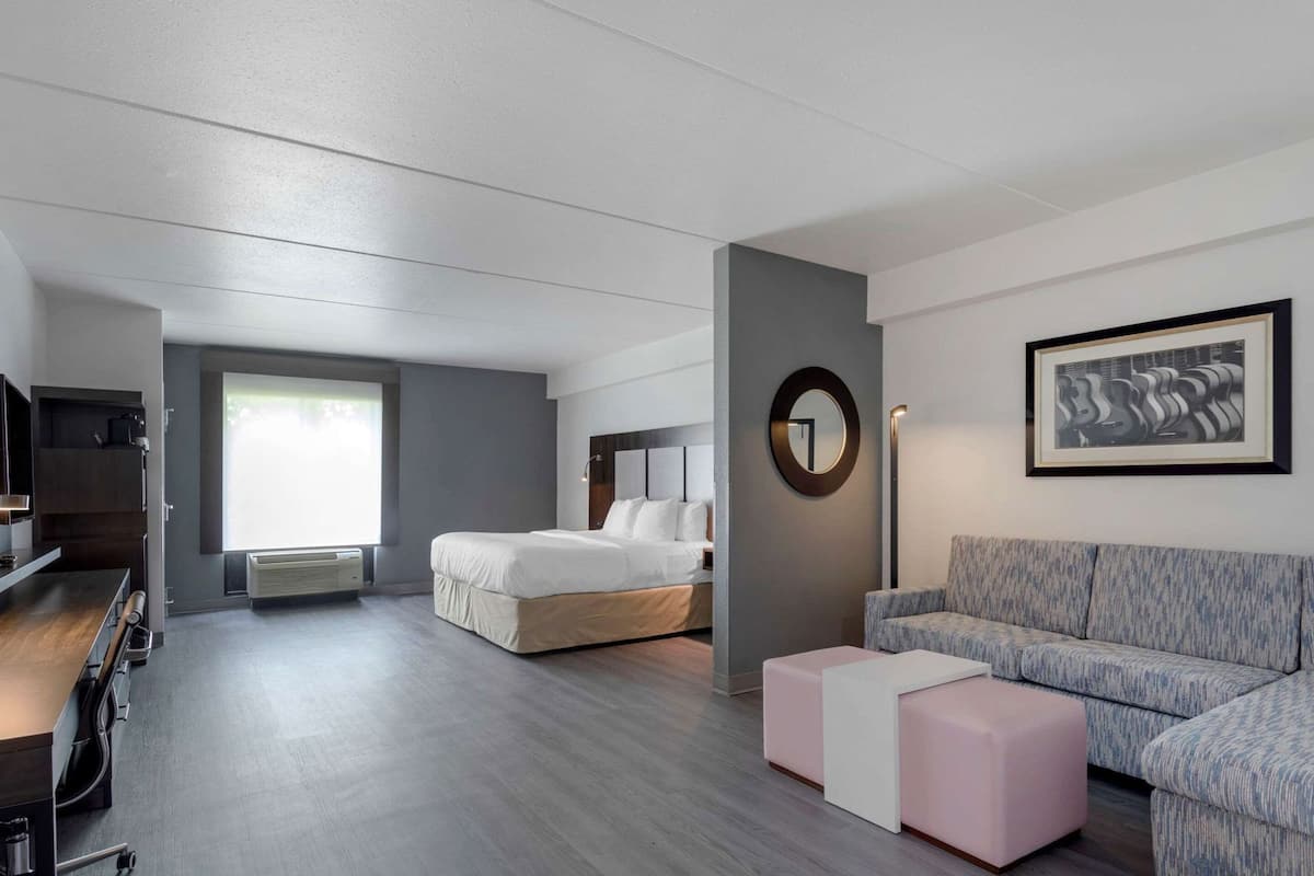 A modern hotel room with a bed, a sofa, a desk, and a large window.