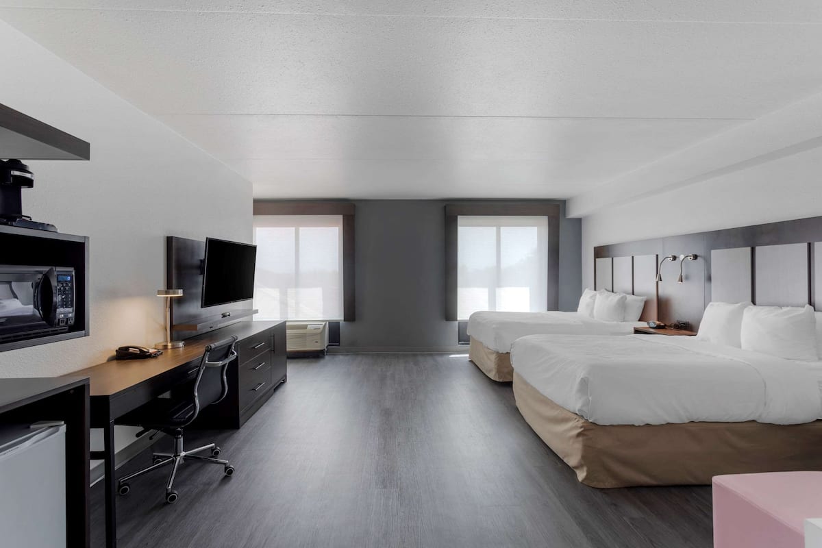 A modern hotel room with a desk, television, and two beds.
