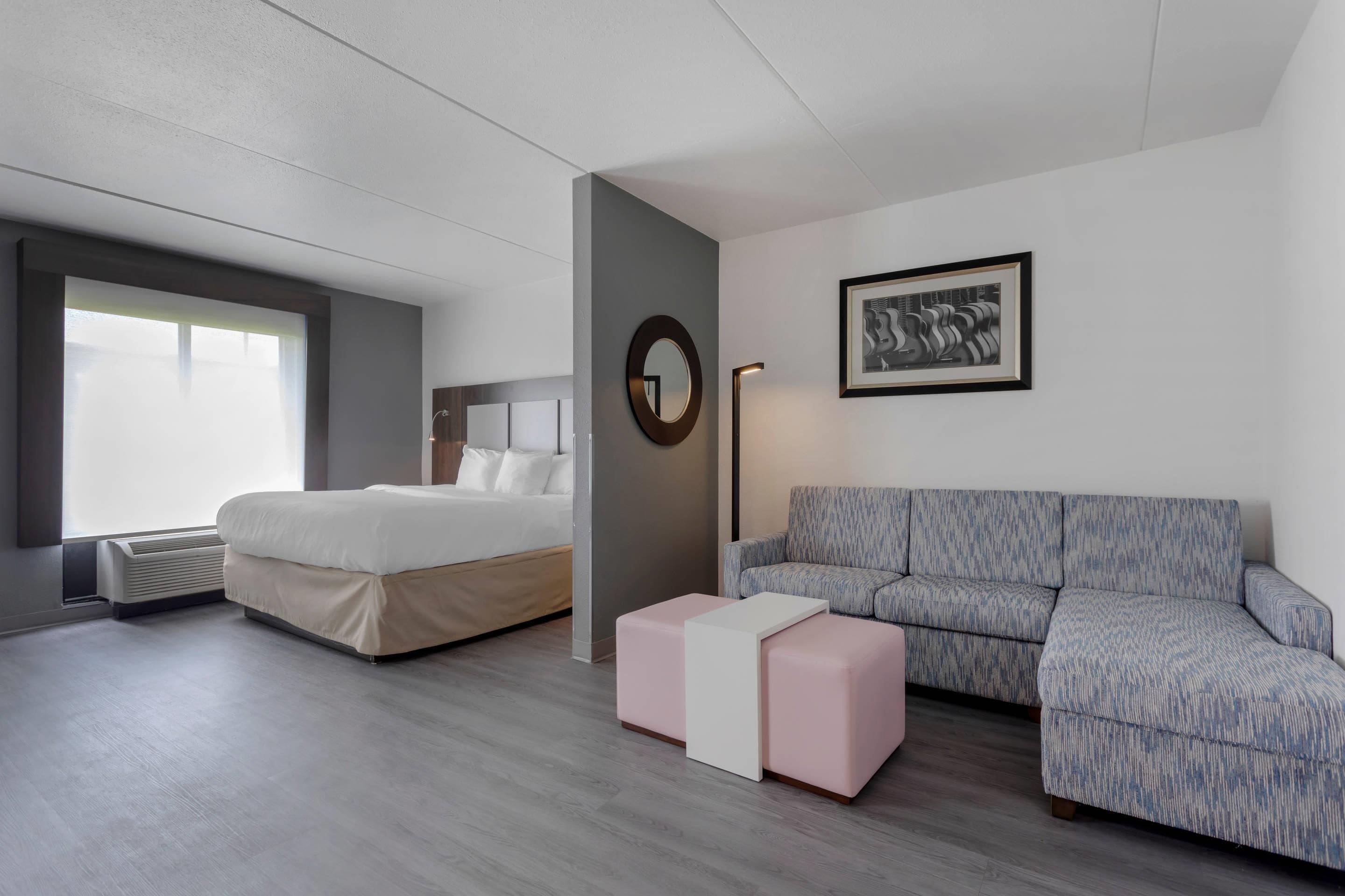 A modern hotel room with a bed, a sofa, a small table, and a framed artwork on the wall.