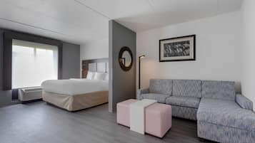 A modern hotel room with a bed, a sofa, a small table, and a framed artwork on the wall.