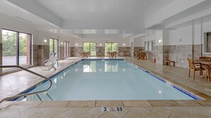 Una piscina interior con agua cristalina, suelo de baldosas y mobiliario de madera alrededor.