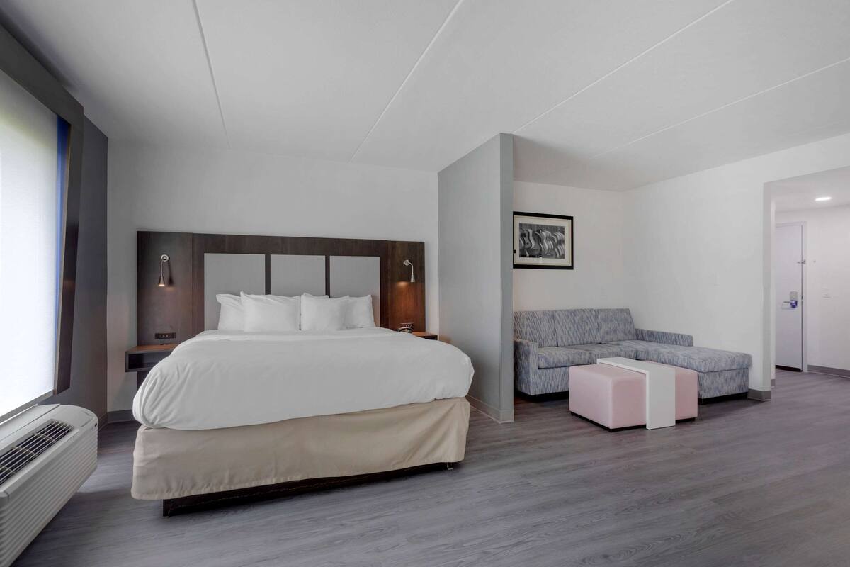 A modern hotel room with a large bed, a gray sofa, and a small table.