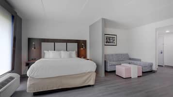 A modern hotel room with a large bed, a grey sofa, a small table, and a framed picture on the wall.