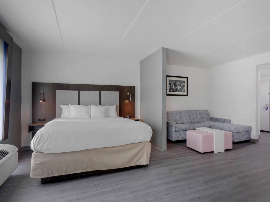 Una habitación de hotel moderna con una cama grande, un sofá gris, una mesita pequeña y un cuadro en la pared.