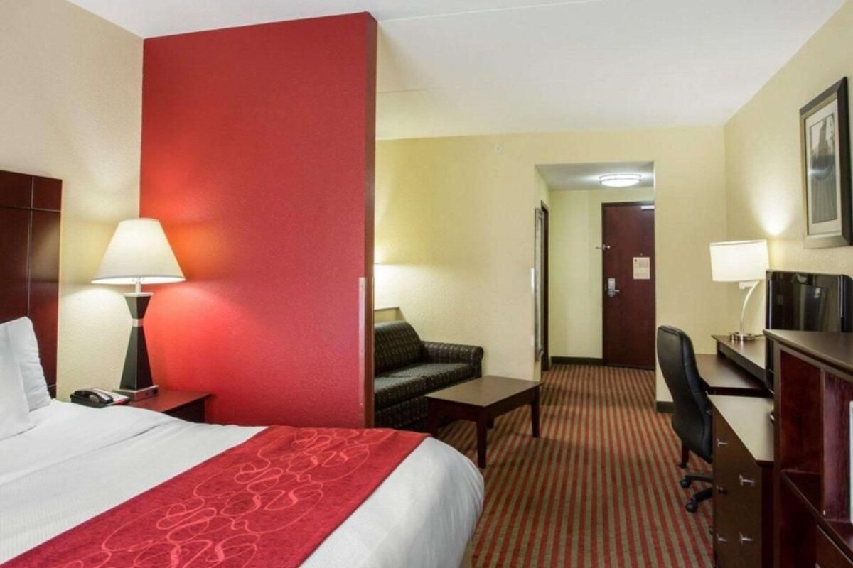 A hotel room with a bed, desk, chair, and a mirror.