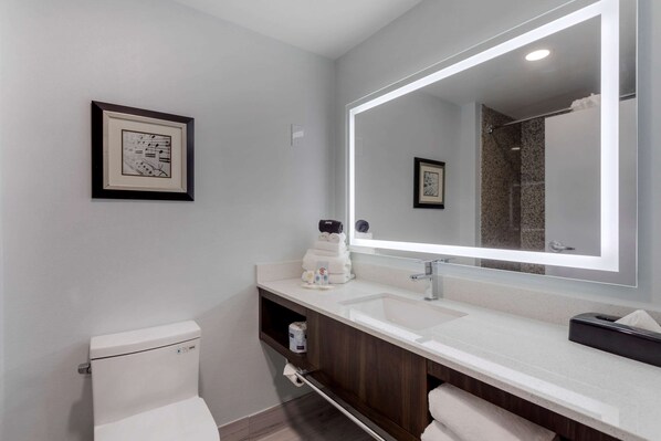 A modern bathroom with a large mirror, white toilet, and a vanity with a sink and towel rack.
