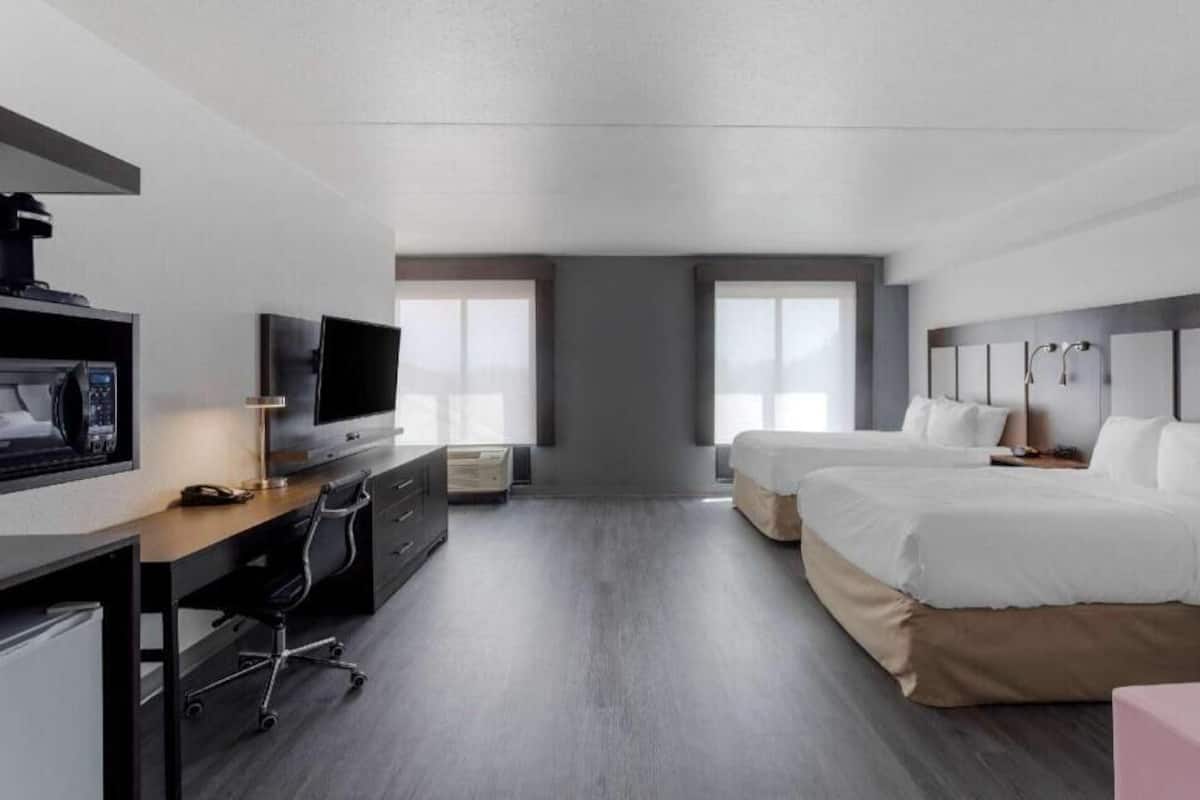 A modern hotel room with a desk, TV, two beds, and large windows.