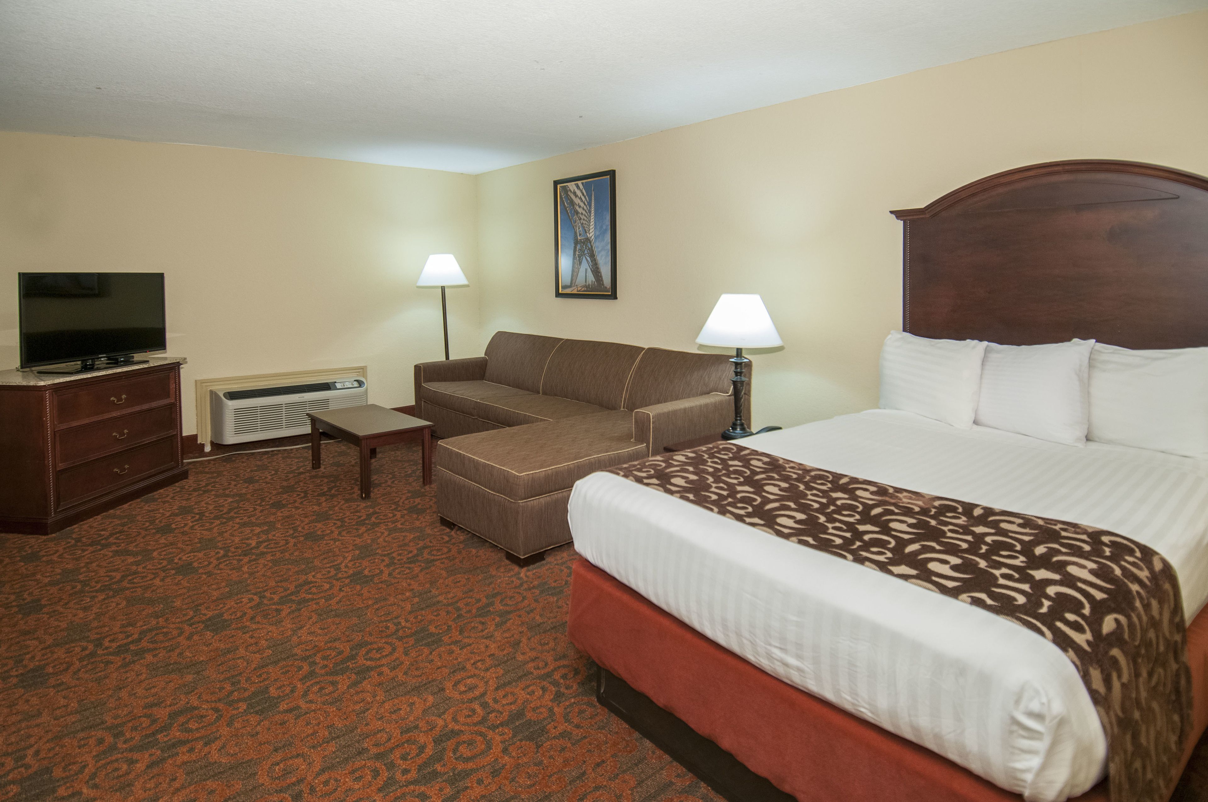 A hotel room with a bed, a sofa, a TV, a desk, and two lamps.