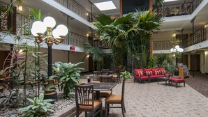 A multi-level atrium with indoor plants, a red sofa, and a dining area with tables and chairs. - Governor's Suites Hotel Oklahoma City Airport Area (Oklahoma City)