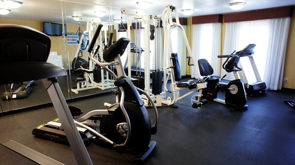 Un gimnasio con máquinas de cardio, máquinas de pesas y un muro de espejos.