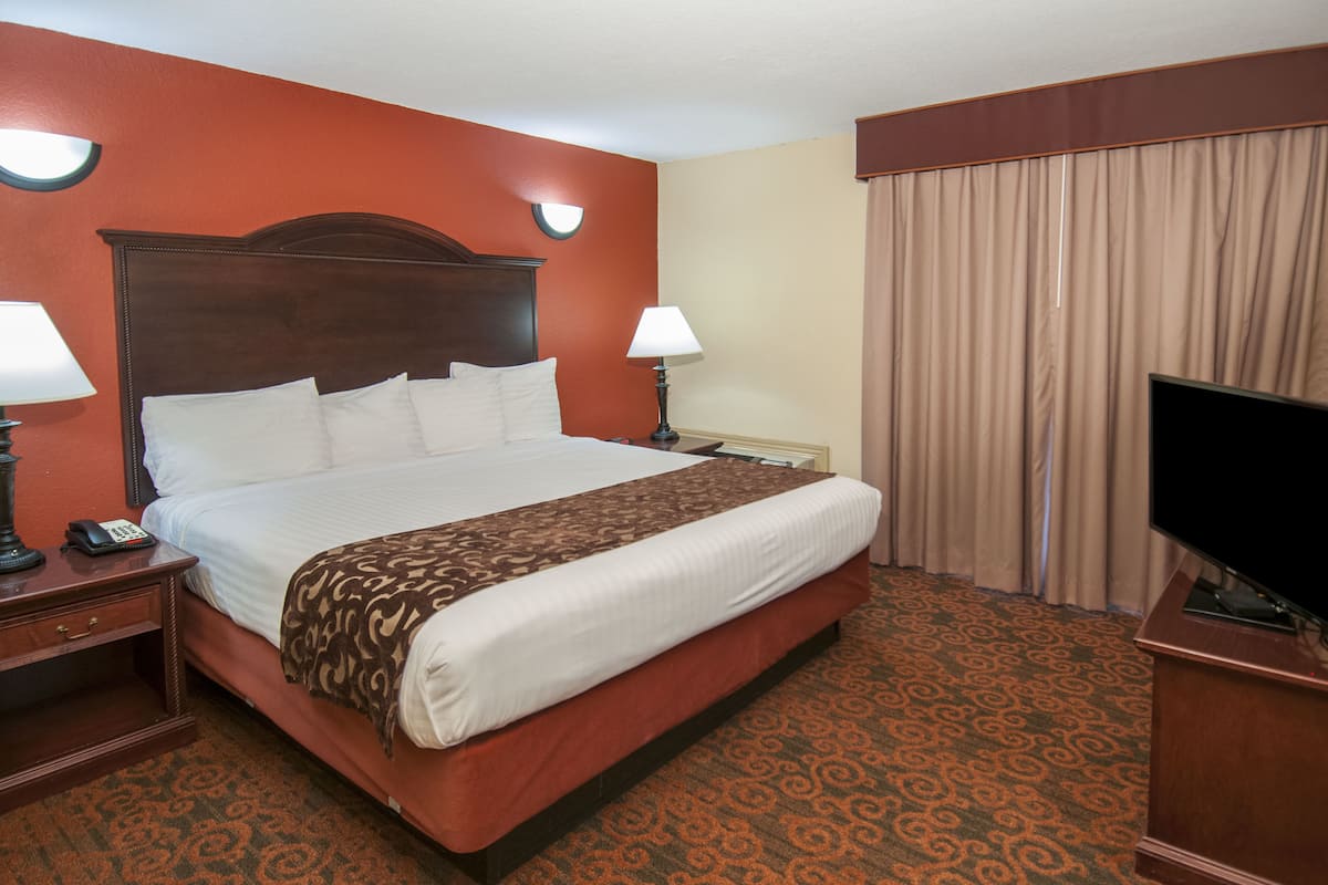 A hotel room with a large bed, two bedside lamps, a flat-screen TV, and a curtain on the window.