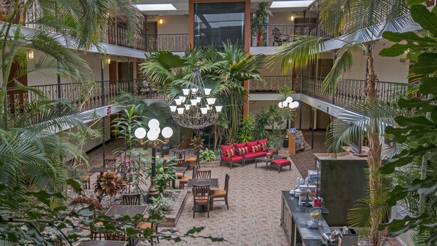 A multi-level atrium with a central seating area, surrounded by lush greenery and a chandelier. - Governor's Suites Hotel Oklahoma City Airport Area (Oklahoma City)