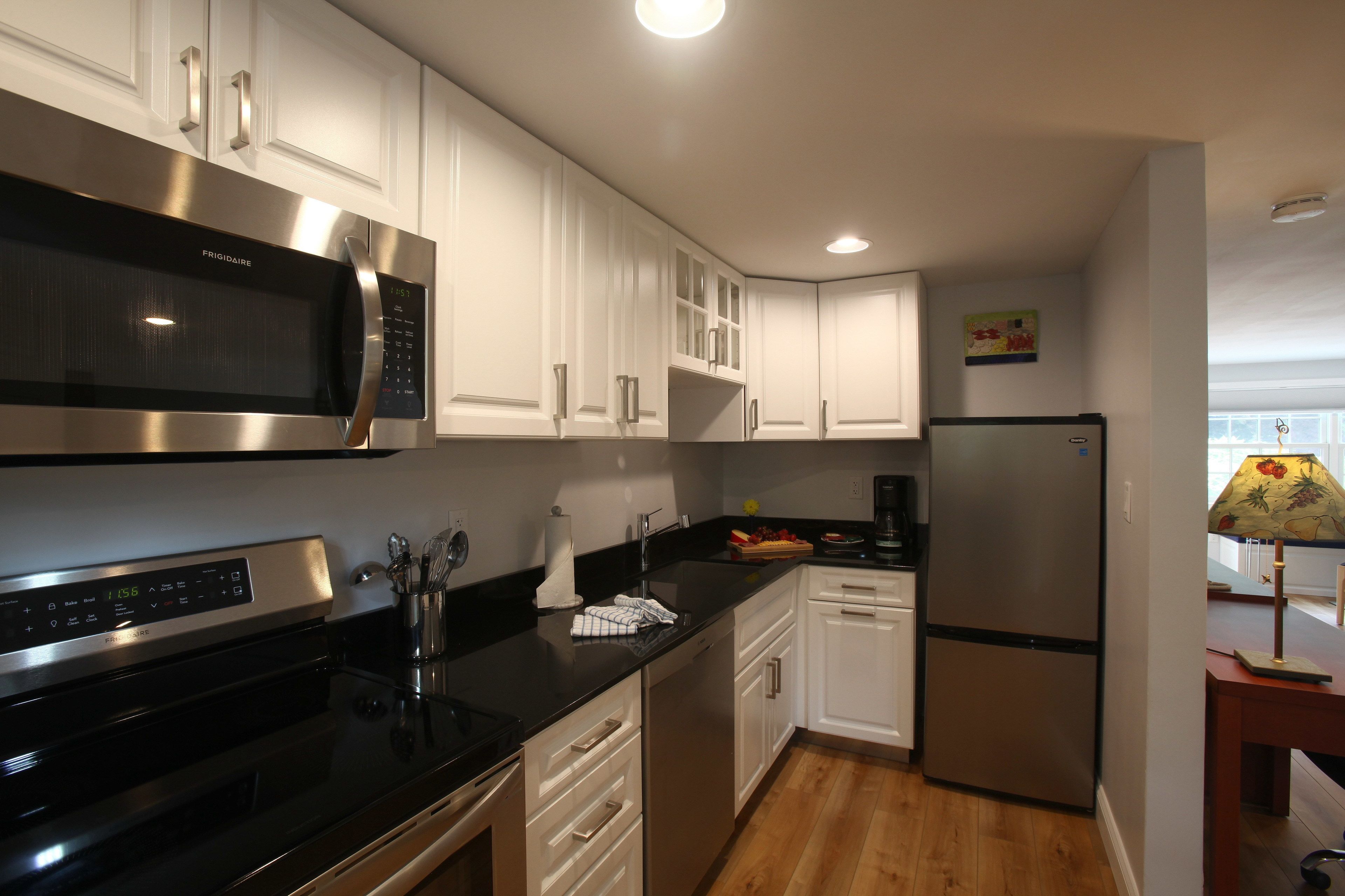 A modern kitchen with white cabinets, stainless steel appliances, and wooden flooring.