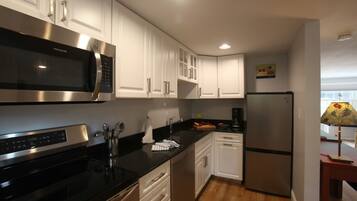 A modern kitchen with white cabinets, stainless steel appliances, and wooden flooring.