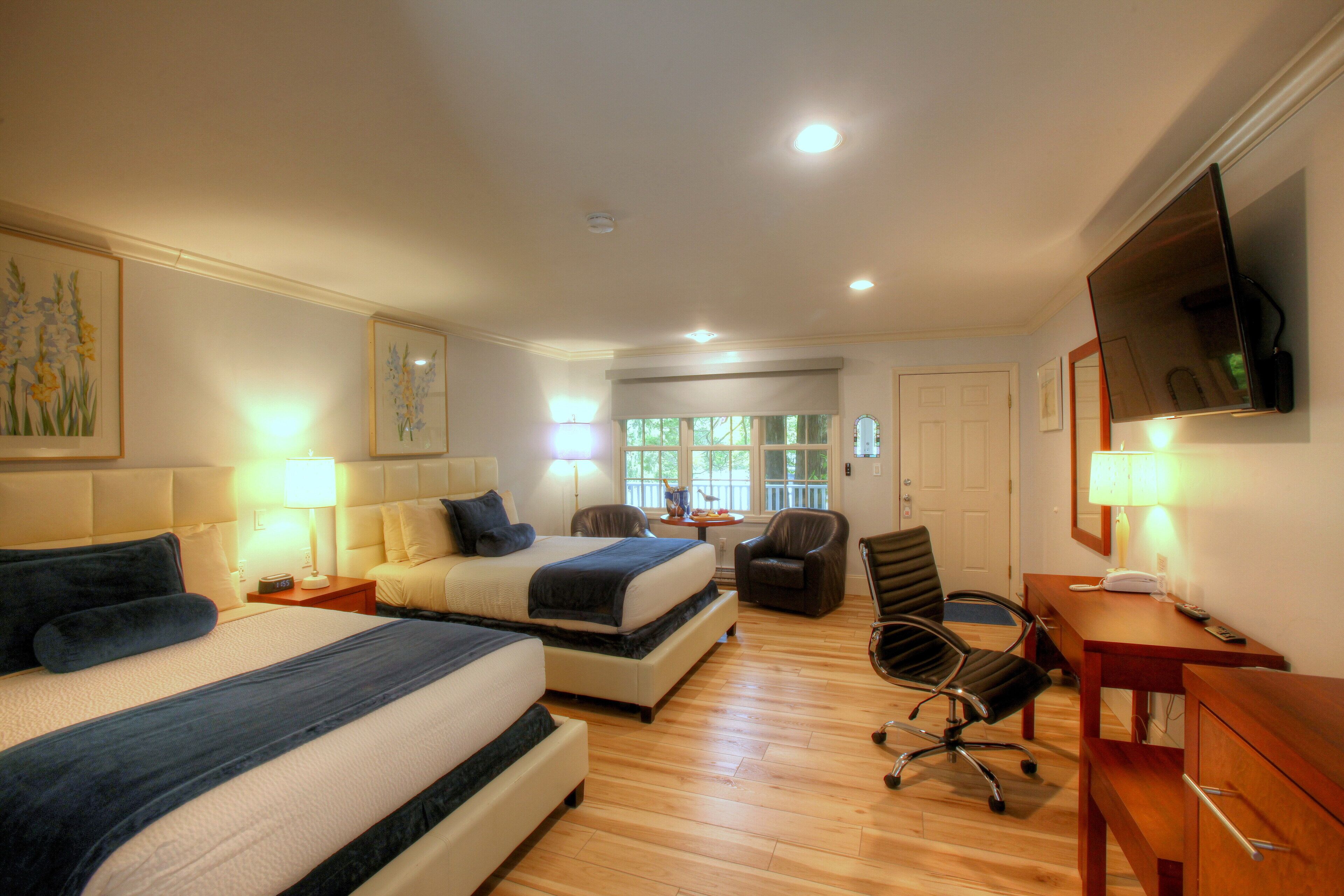 A hotel room with two beds, a desk, a chair, and a TV.