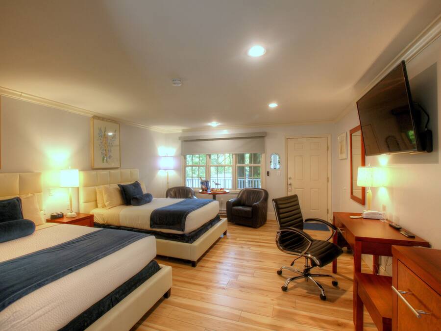 A hotel room with two beds, a desk, a chair, and a TV.