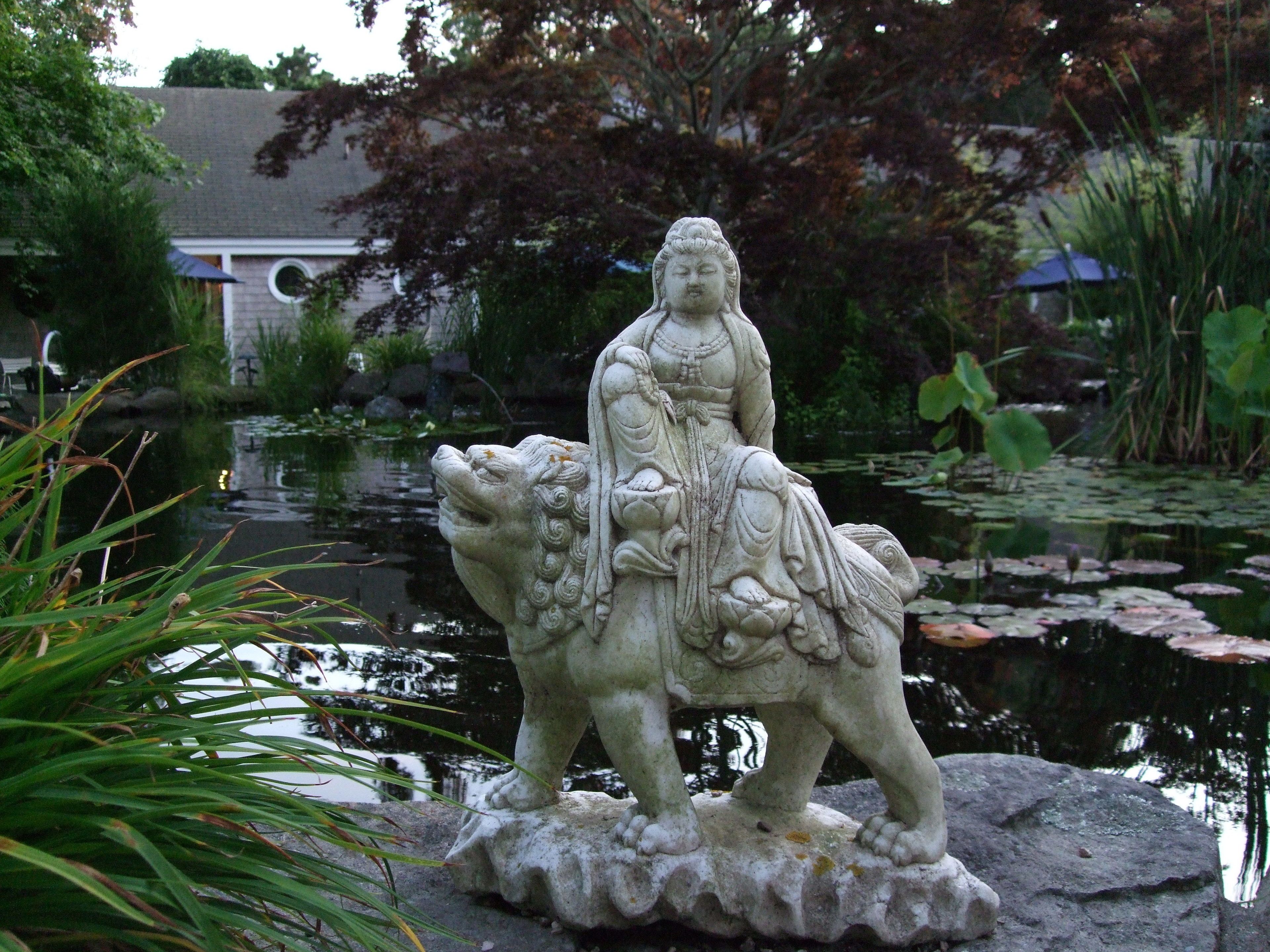 A stone statue of a figure on a horse by a pond.