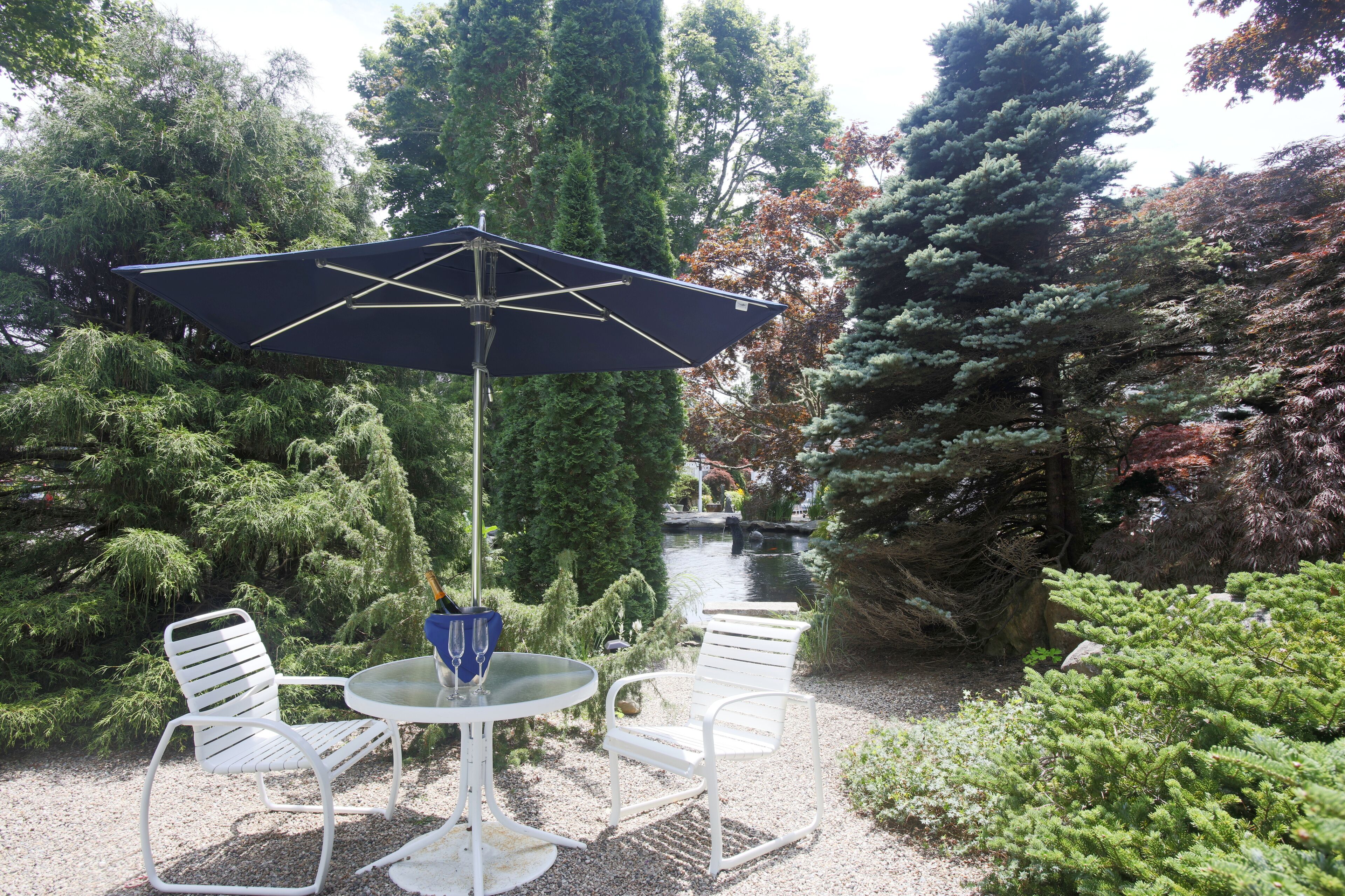 A garden patio with a round table, two white chairs, and a blue umbrella.