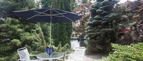 A garden patio with a round table, two white chairs, and a blue umbrella.