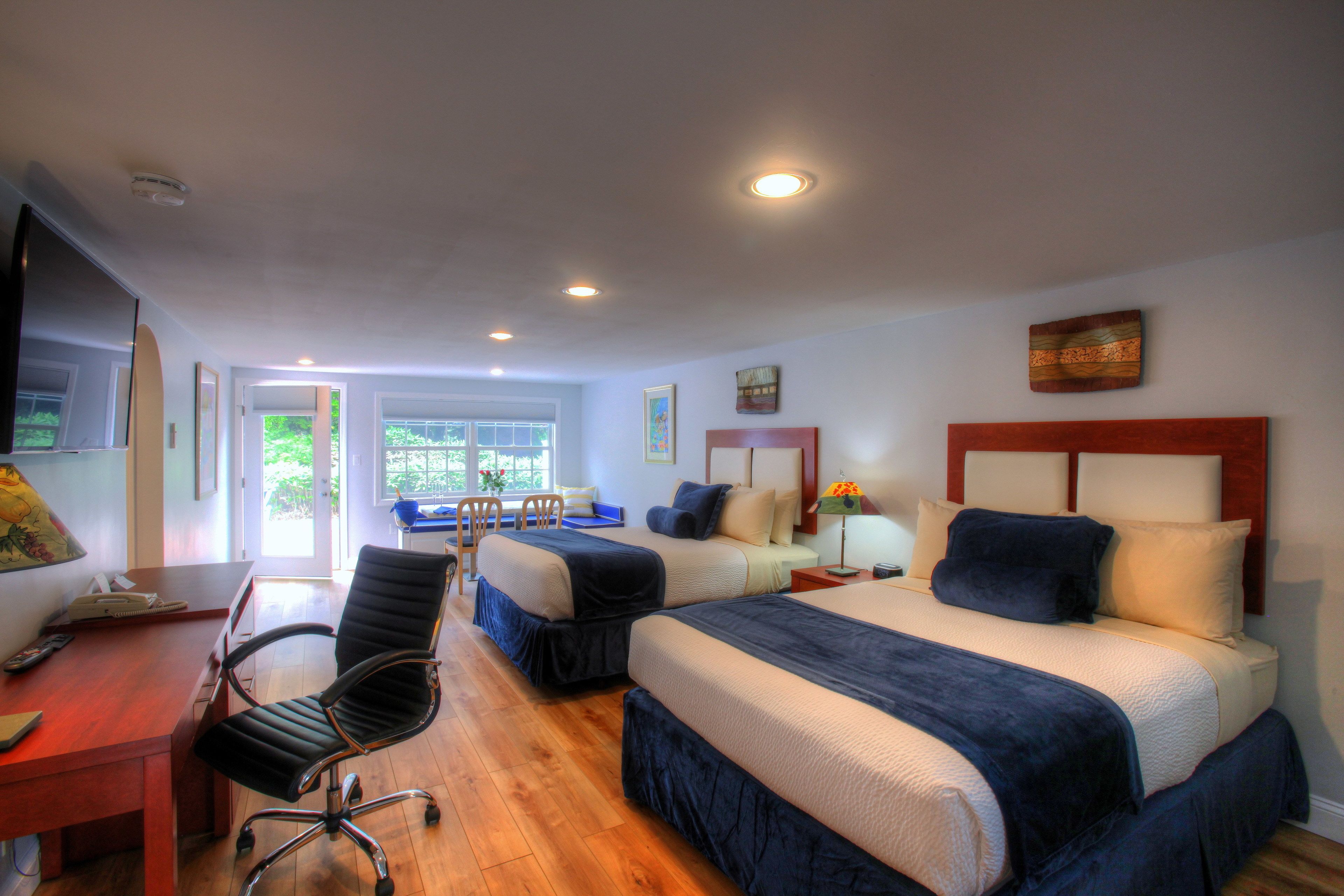 Une chambre d’hôtel avec deux lits, un bureau et une chaise. Une fenêtre offre une vue sur la verdure environnante.