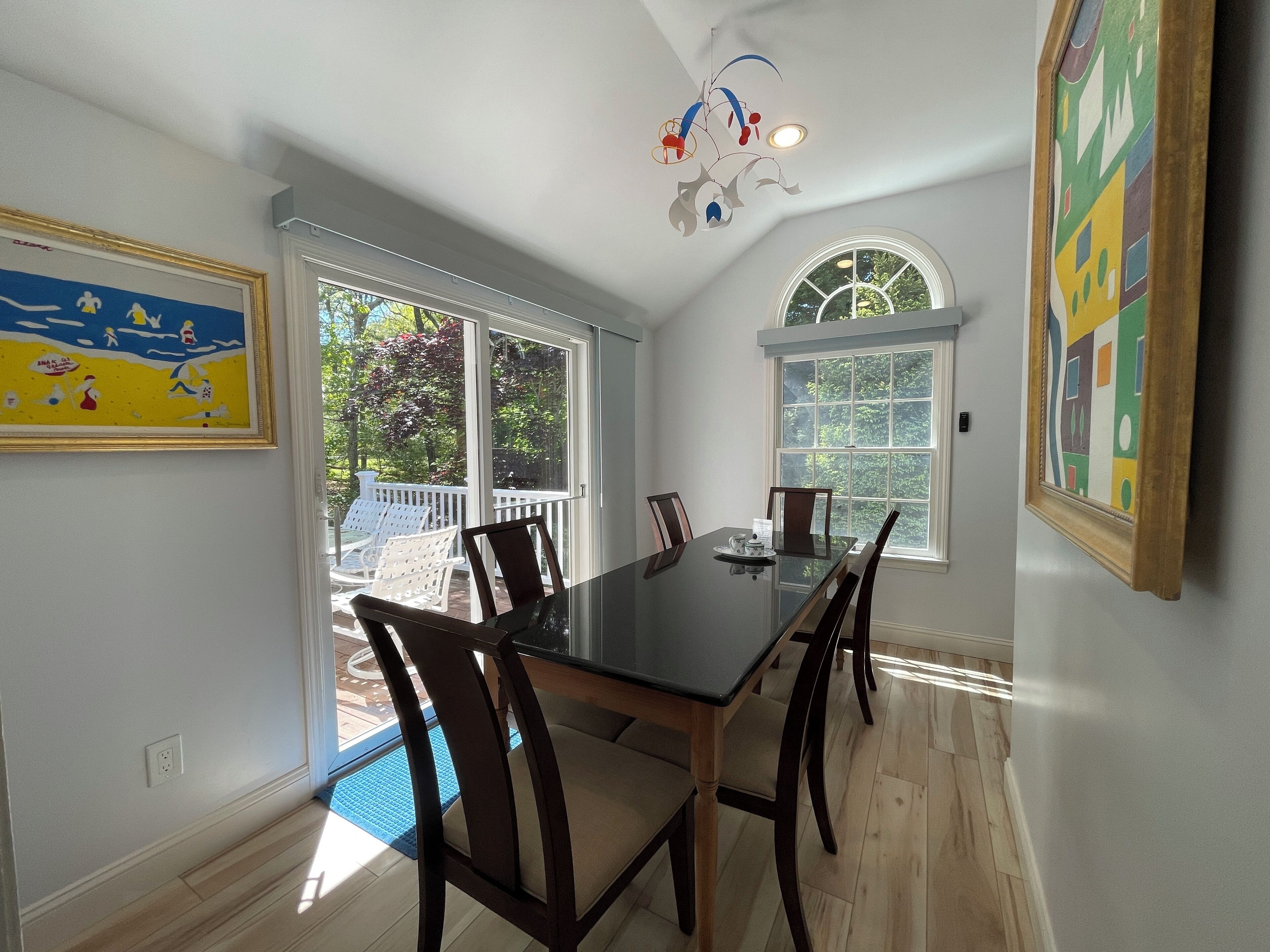 A dining area with a glass table, wooden chairs, and a view of the outdoors through large windows.